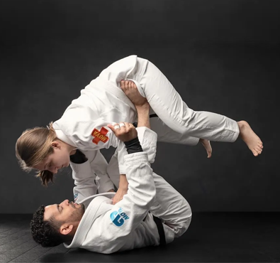 Two adults practicing Brazilian Jiu Jitsu ground technique with one lifting the other during grappling training in white gis